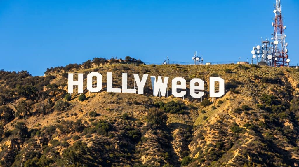 Hollyweed inspireret bjergskilt i Hollywood stil på solbelyst bakke under klar blå himmel.