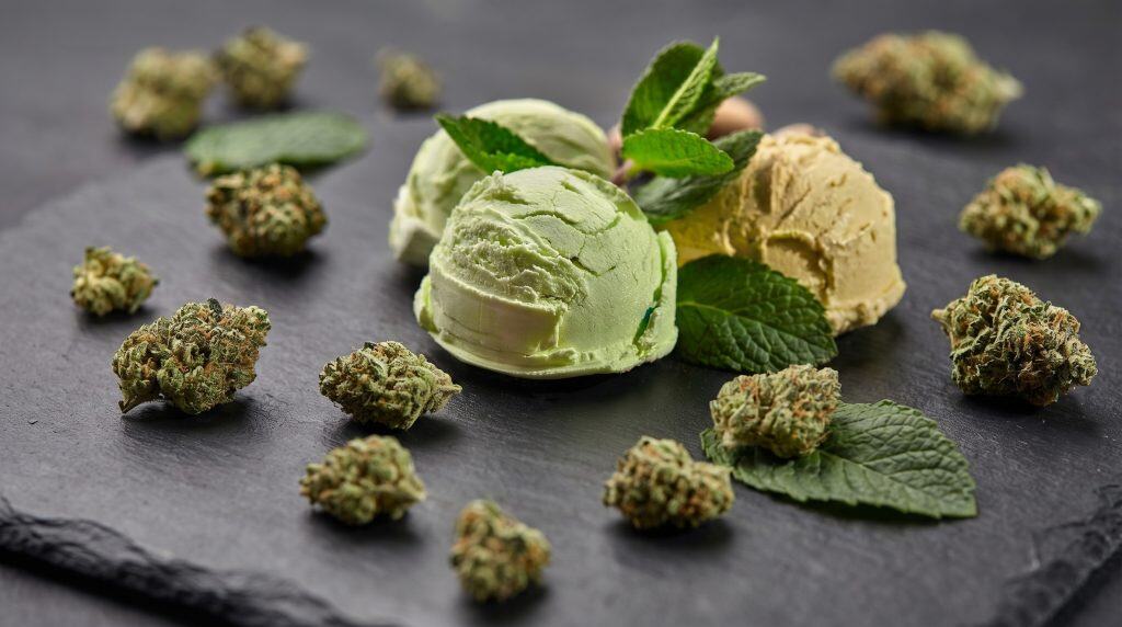 Gelato topskud arrangeret omkring kugler af grøn og cremet is med mynteblade på mørk baggrund, som fremhæver strainens dessertinspirerede profil.