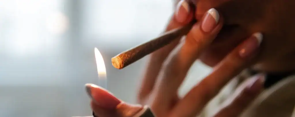 Nærbillede af person, der tænder en Bubba Kush joint med lighter i blødt, varmt lys.

