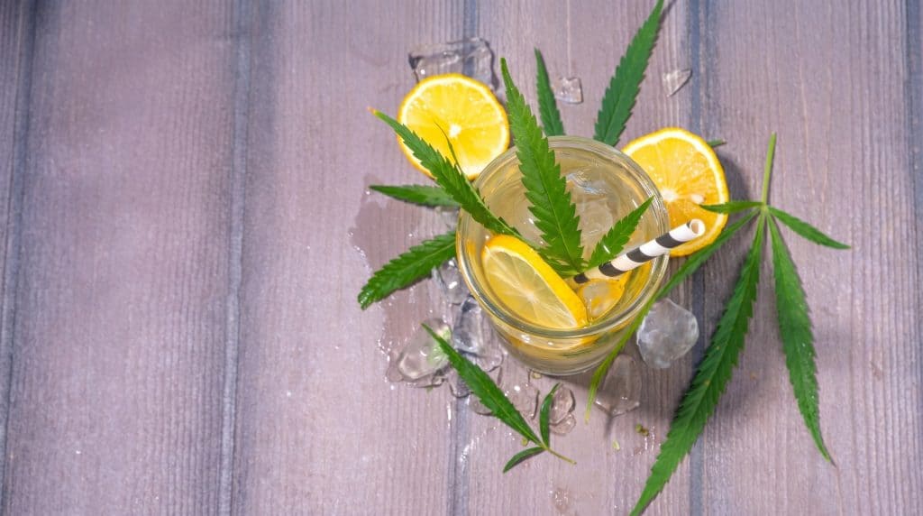 Lemonade inspireret drink med citronskiver, isterninger og grønne hampblade på træbord, som fremhæver strainens friske og citrusprægede profil.