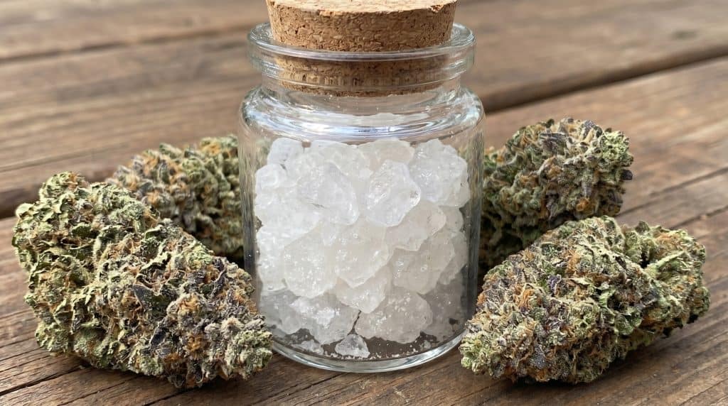 THCa diamonds i glasbeholder med store, klare krystaller omgivet af topskud på rustikt træbord.