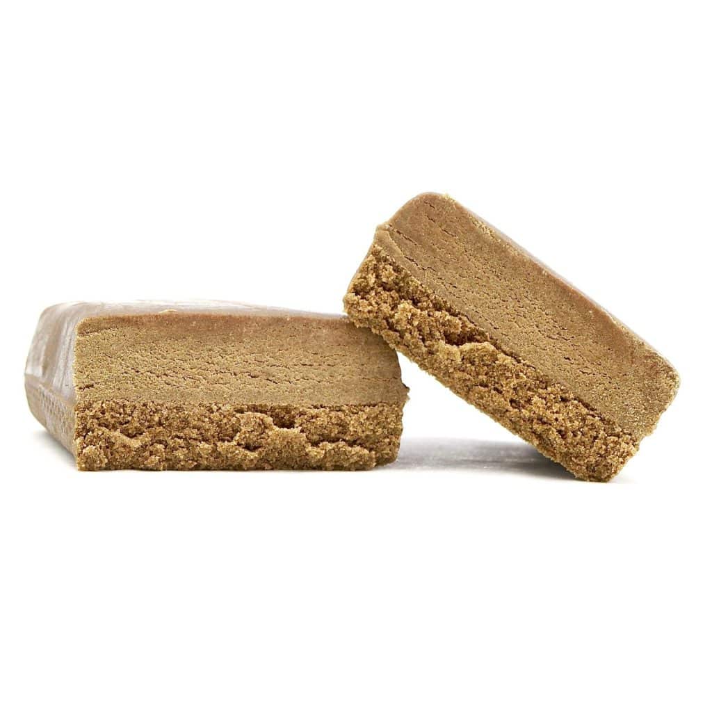 Bubble hash THCa hash i to delte stykker med mørk yderside og blød, porøs struktur på lys baggrund.