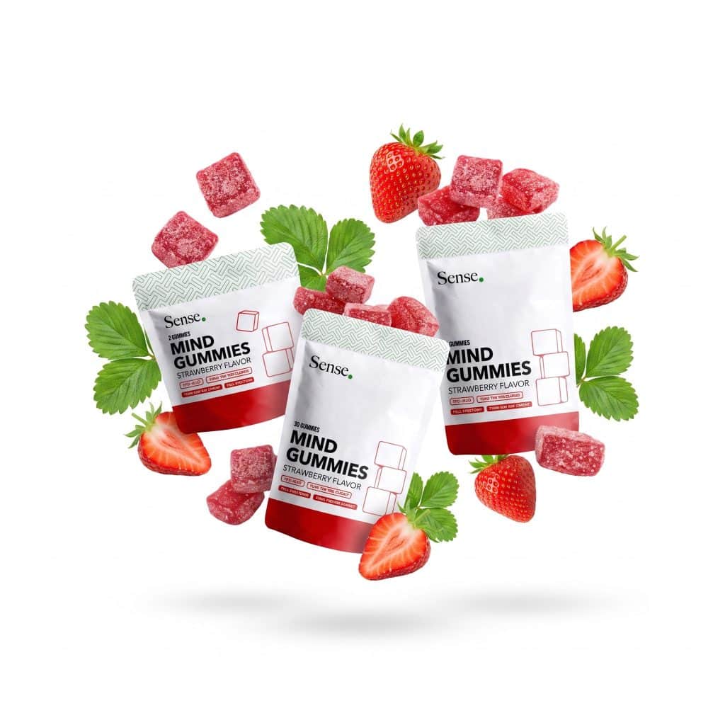 Mind Gummy Strawberry Flavor i flere pakkestørrelser omgivet af jordbær, grønne blade og røde gummies på lys baggrund.
